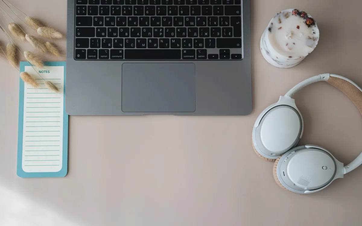 A laptop, headphones, and a notebook arranged on a small desk.