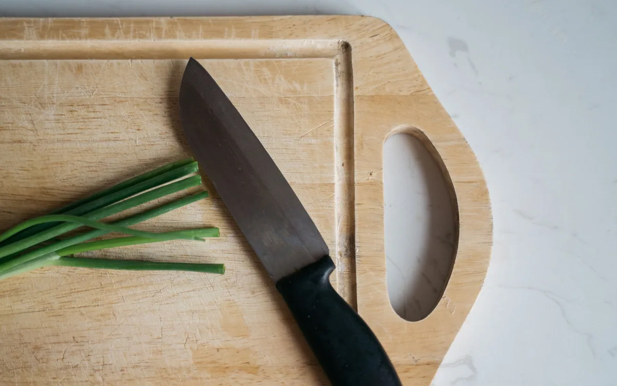A knife and chopped green onions on a wooden cutting board.
