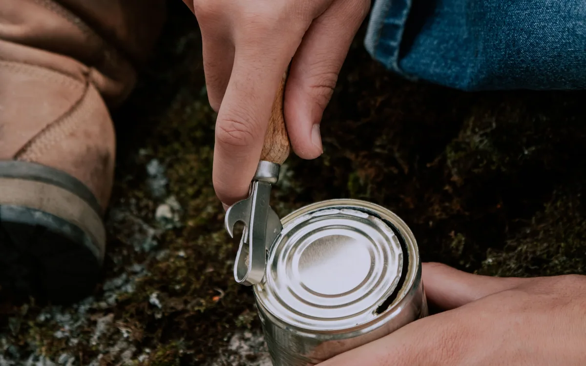 Hands using a manual opener to open a tin can.