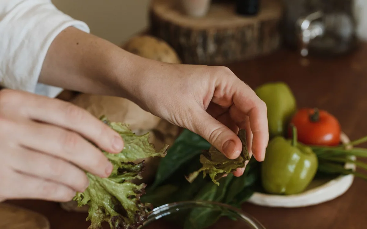 Hands tearing lettuce in a kitchen.