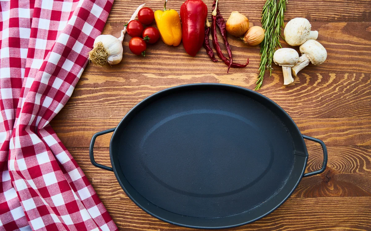 An empty black two-handled pan on a table beside ingredients.