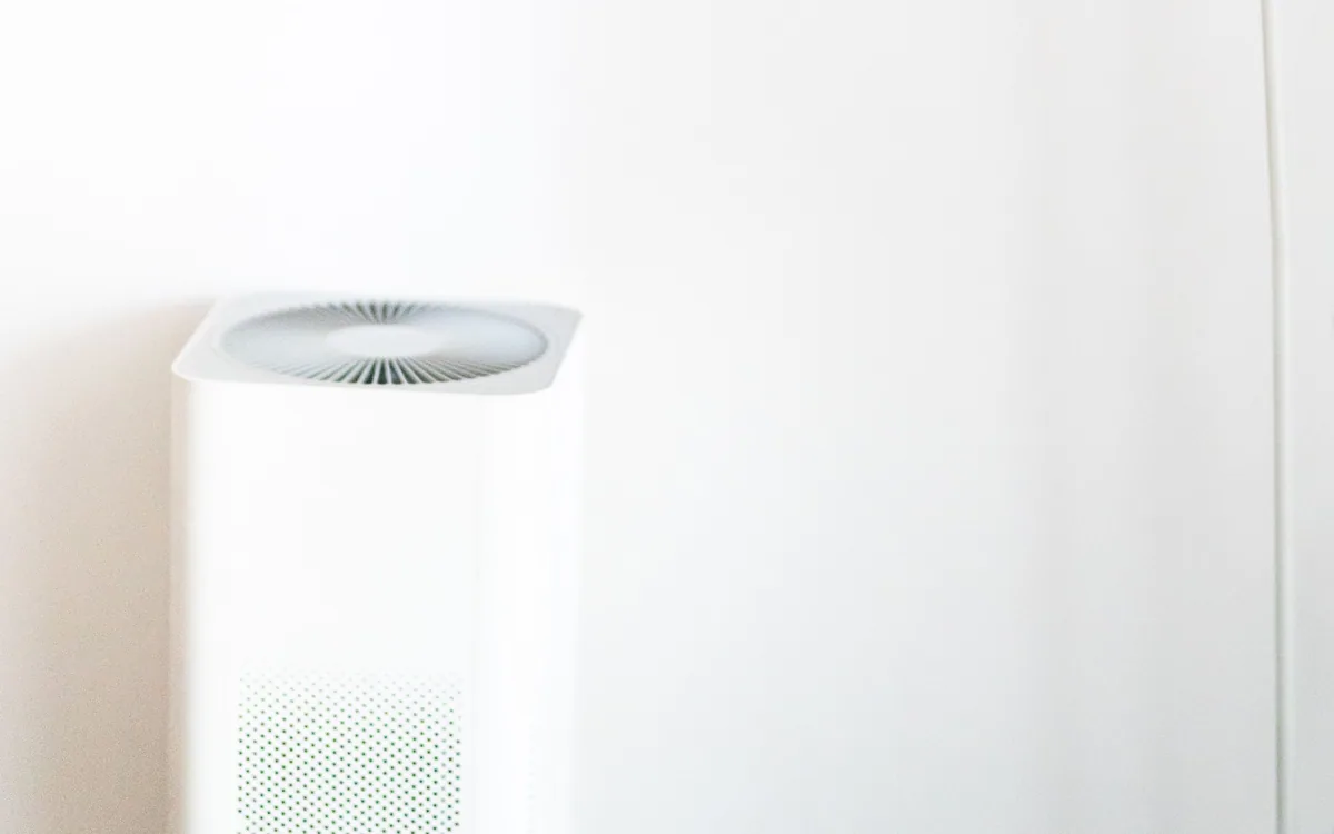 An air purifier beside a floor lamp against a light wall.
