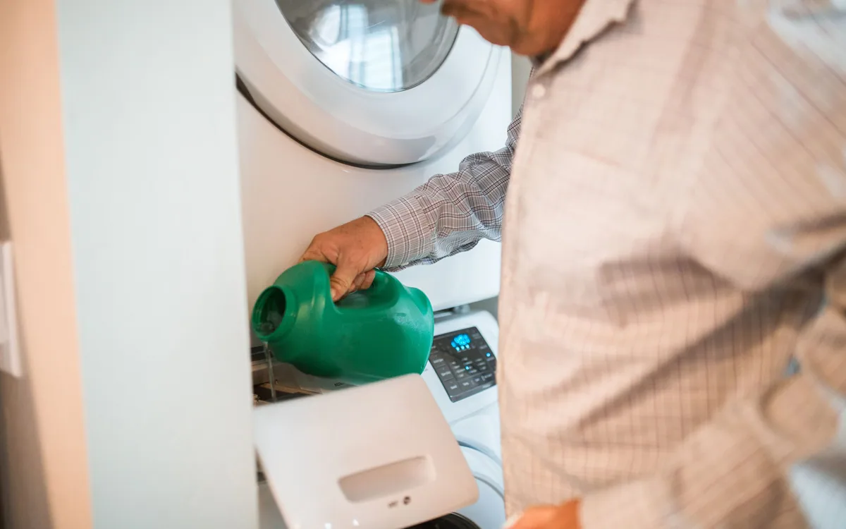 A person pouring laundry detergent beside a washing machine.