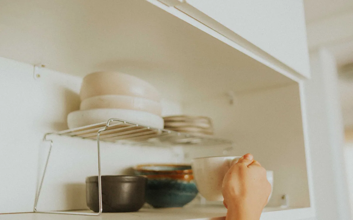 An open kitchen cabinet holding neatly stacked mugs and dishes.