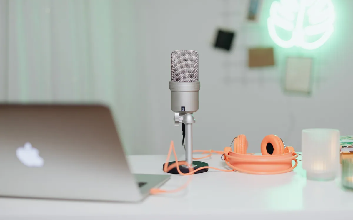 A desktop microphone beside a laptop and headphones.